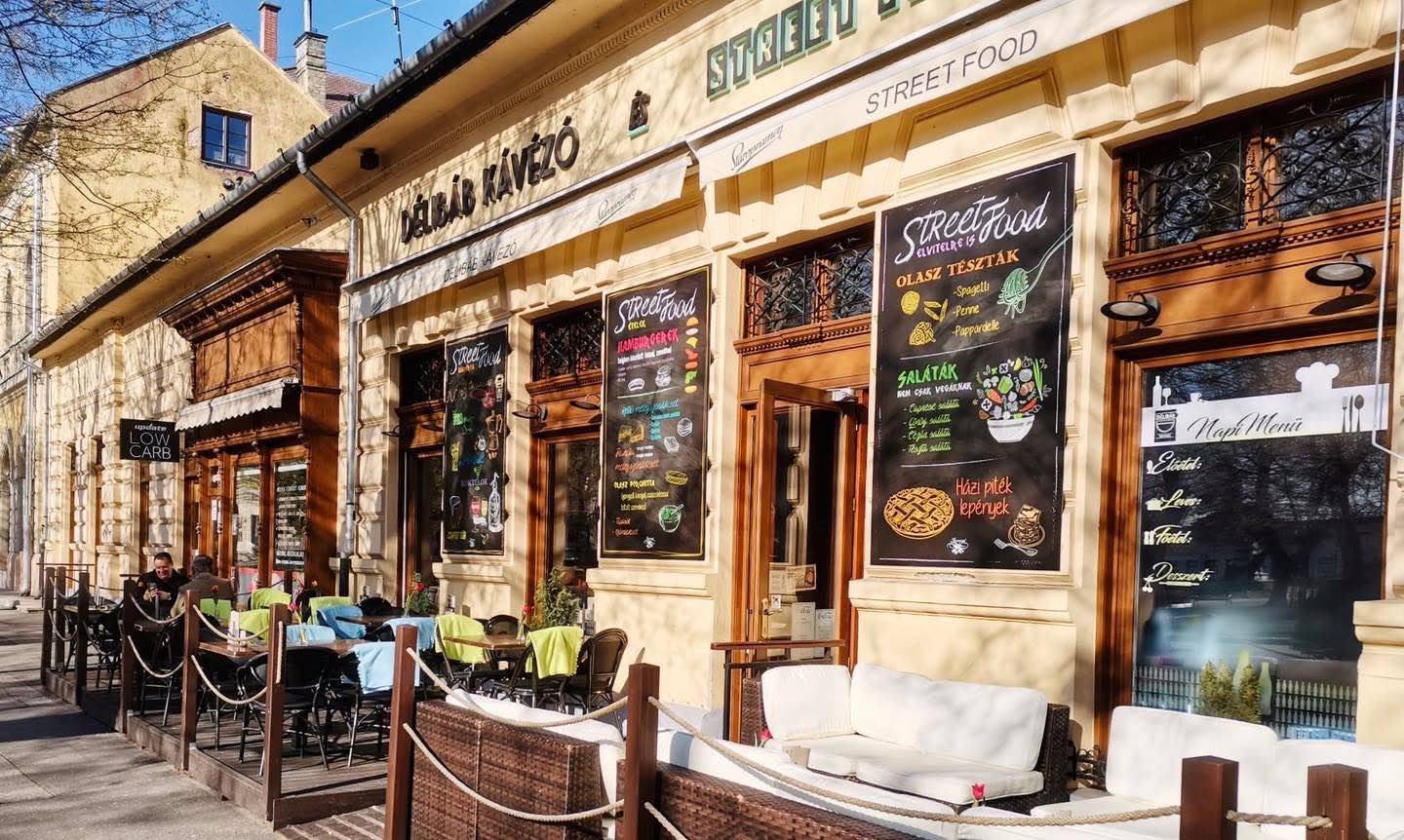 A Délibáb Kávézó és Street Food sárga műemlék-homlokzata a ceglédi Szabadság téren, terasszal és krétatáblás étlapokkal
